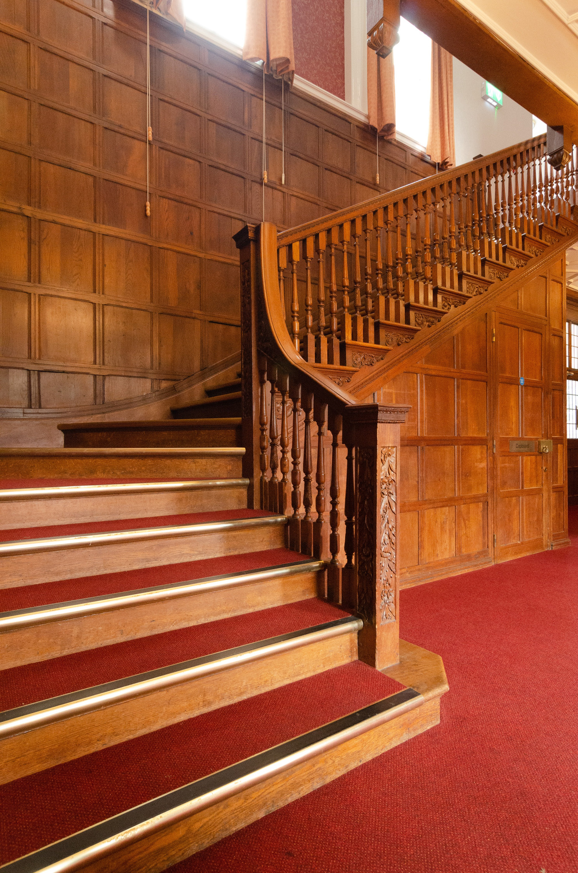 ornate wooden stairs in a large room with a deep red carpet